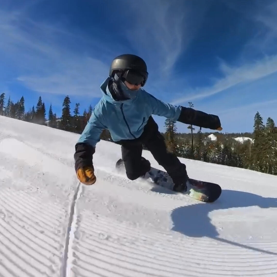 Chris Ball, a 10 year snowboard instructor showing off his carving skills at Homewood mountain resort on his favorite snowboard, Neversummer Industries, protosynthesis. He's wearing a light blue jacket and black pants.